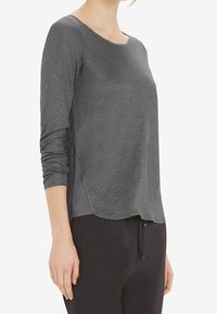 Graues Langarmshirt mit rundem Halsausschnitt, leicht geschwungenem Saum und Seitenpaneeldetails, aus einem leichten, weichen Stoff gefertigt.