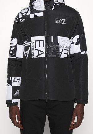 Black and white puffer jacket featuring a geometric pattern, logo accents, a zip front, and elastic cuffs. Textured fabric.