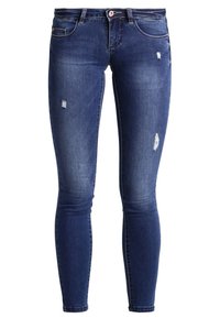 Jeans ajustados de mezclilla azul oscuro, con desgastes y pequeños desgarros. Diseño clásico de cinco bolsillos con cierre de botón y pasadores para cinturón.