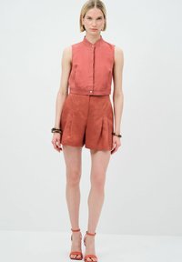 Completo in lino color ruggine composto da un top senza maniche con colletto e pantaloni corti a vita alta con pince, abbinati a sandali con cinturini.