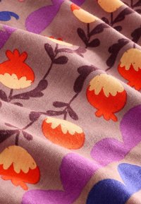 Tissu doux avec un motif de fruits rouges et crème ressemblant à des grenades, feuilles violettes et bleues sur un fond violet clair.