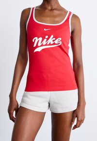 Röd linne i ribbat material med en vit Nike-logotyp. Ihopkopplad med ljusgrå shorts. Har rund halsringning och breda axelremmar.