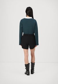 Tee s dolgimi rokavi v morsko zeleni barvi z belim ovratnikom, v kombinaciji z visokimi črnimi šortami. Črne škornje do kolen odlikujejo sponke in teksturirana površina.