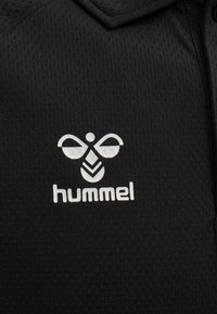 Sort polo-shirt lavet af tekstureret stof med et hvidt logo, featuring et bi-design og ordet "hummel" nedenunder.