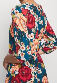 Blumenkleid mit blauem Hintergrund und roten, rosa und weißen Blumen. Es hat kurze Puffärmel und einen Rückenschlitz.