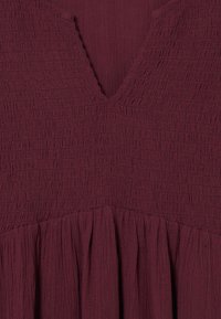 Robe bordeaux en tissu texturé et froissé avec un décolleté en V et des plis froncés à l'ourlet. Matériau doux et léger.