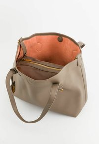 Beige läder tote-väska med en mjuk textur, har ett orange mockainredning, en ficka med dragkedja och detaljer i guldton.