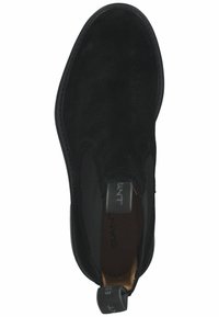 Bottine en suede noire avec des panneaux latéraux élastiques, bout arrondi et languette de tirage. Texture lisse avec un minimum de points de couture.