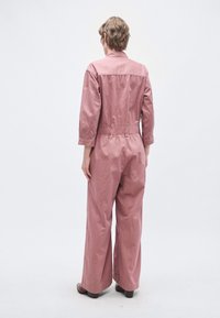 Rózsaszín pamut overál hosszú ujjakkal, rugalmas derékkal és bő szárakkal. A dizájn gallérral és hátsó vállvarrás részlettel rendelkezik.