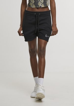 Személy fekete, zsinóros rövidnadrágot visel, melyen fehér logó van a bal combon, fehér zoknit, fehér tornacipőt, és rövidített kígyómintás felsőt.