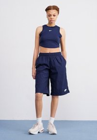 Morski crop top s malim logom, uparen s morskim šortsevima do koljena koji imaju bijeli logo; model nosi bijele čarape i svijetle tenisice.