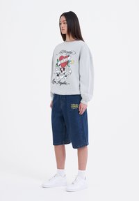 Vaaleanharmaa huppari, jossa on graafinen printti, yhdistettynä polvimittaisiin sinisiin farkkushortseihin. Valkoiset tennarit viimeistelevät asun.