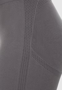Harmaat leggings, joissa on teksturoitu muotoilu, verkko-ompeleet ja sileä kangaspinta. Rakenteessa on erottuvat kuviot ja saumat.
