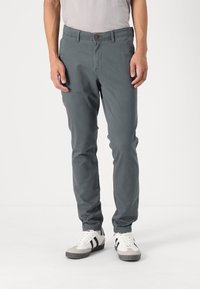 Chinos de algodón grises con un corte ajustado, que presentan un cierre de botón, bolsillos laterales y dobladillos enrollados. Combinados con zapatillas blancas y grises.
