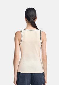 Canotta beige senza maniche con un design aderente, bordi neri lungo il collo e le braccia, e un tessuto liscio e elasticizzato.