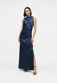 Μακρύ φόρεμα σε ναυτικό μπλε σατέν με στρογγυλή λαιμόκοψη, σούρες στο πλάι και σκίσιμο μέχρι τον μηρό, με απαλό ύφασμα και εφαρμοστή γραμμή.