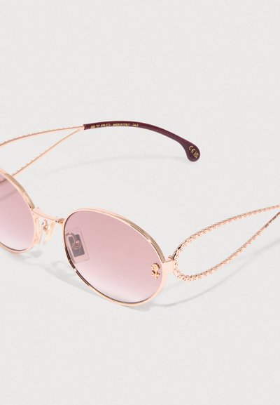 Lentes redondos de gradiente rosa en un marco metálico dorado ornamentado con brazos perlados, puntas de patilla marrones y un pequeño emblema decorativo en la lente derecha.