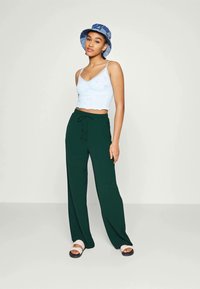Un haut court bleu clair avec un motif texturé, associé à un pantalon ample vert foncé et des sandales blanches. Accessoirisé avec un chapeau seau bleu.