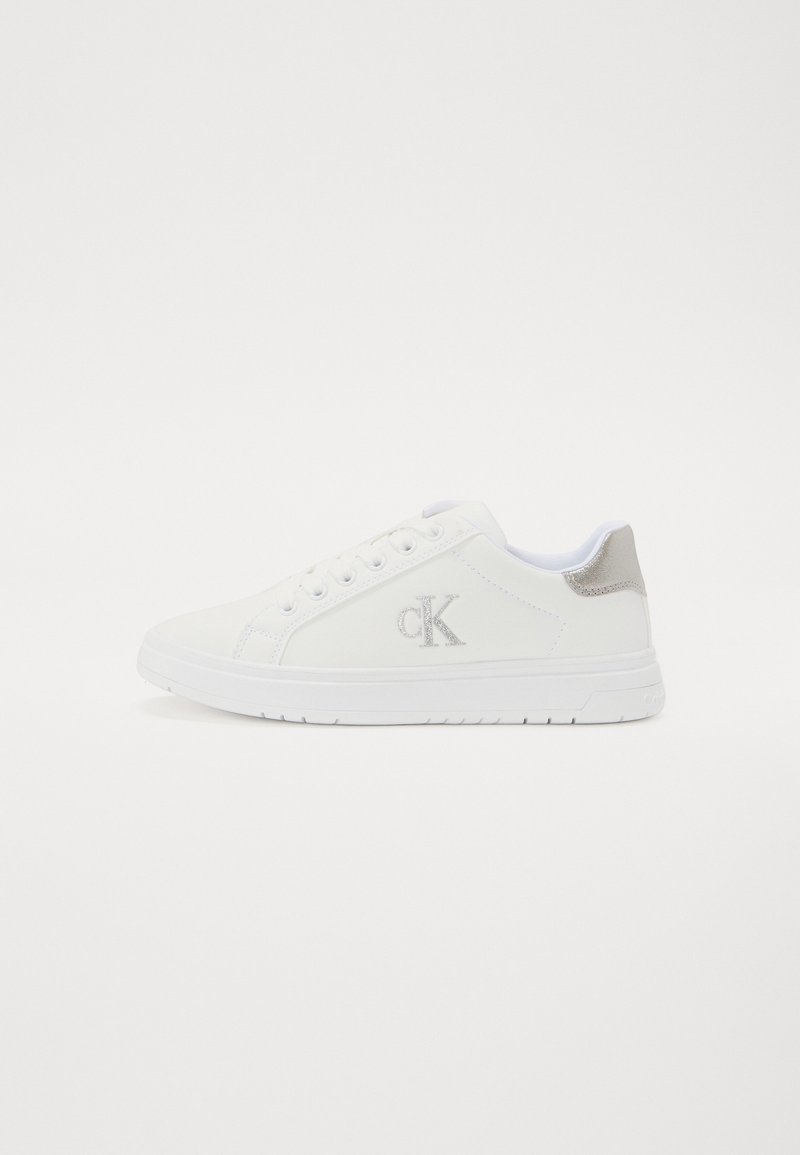 Sapatilhas brancas feitas de material sintético, com uma textura suave, forma arredondada, design com atacadores e logo prateado na lateral.