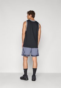Top sin mangas negro, pantalones cortos gris con estampados y acentos negros, calcetines negros y zapatillas deportivas negras. Capturado desde atrás, enfocado en la ropa.