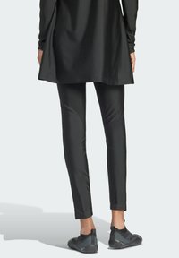 Crne sportske tajice u kombinaciji s dugim crnim topom, s glatkom teksturom, uskim fitom i mrežastim detaljima na cipelama.