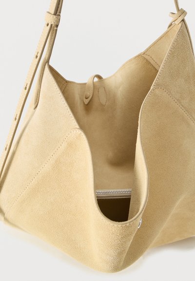 Μαλακή τσάντα ώμου από μπεζ σουέντ με ρυθμιζόμενο λουράκι, ανοιχτό άνω μέρος και ορατή εσωτερική τσέπη με φερμουάρ.