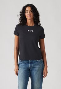 Melnas īsām piedurknēm T-krekls ar baltu "LEVI'S" logo, apaļš kakla izgriezums, piegulošs dizains, apvienots ar gaiši ziliem džinsiem. Mīksts kokvilnas materiāls.