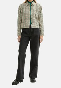Camicia di flanella a scacchi nei colori beige, verde e nero, con un taglio cropped e taschino frontale, abbinata a jeans neri a vita alta e scarpe chunky nere.