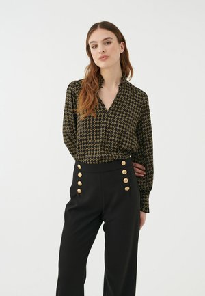 Schwarze Bluse mit goldenem geometrischem Muster, mit einem Schnittkragen und langen Ärmeln, kombiniert mit schwarzen hoch taillierten Hosen mit goldenen Knopfakzenten.
