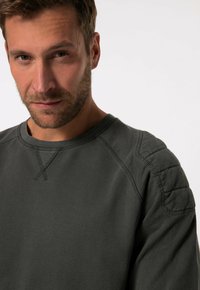 Donkergroene sweatshirt met een ronde hals, geribbelde manchetten en een gestructureerd schouderdetail. Gemaakt van zachte, gladde stof met zichtbare stiksels.