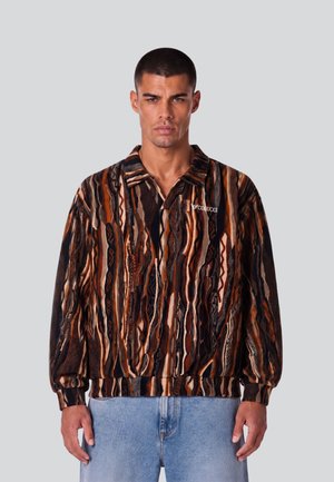 Uomo che indossa un maglione multicolore marrone, nero e arancione con collo e jeans azzurri.