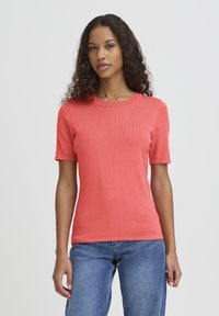 T-shirt corail à manches courtes avec côtes, col rond, coupe ajustée et texture lisse, assorti à un jean denim bleu clair.