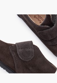 Pantofi din piele întoarsă maro închis, cu formă rotunjită, dotati cu o curea Velcro și un design minimalist. Textură moale cu o talpă durabilă.