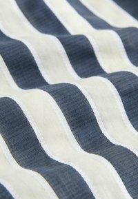 Tissu rayé avec des bandes alternées de bleu marine et de crème, présentant un tissage texturé et des coutures blanches uniformes le long des bords.