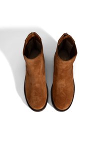 Bottines en daim marron avec une texture lisse, panneaux élastiques sur les côtés et une semelle en caoutchouc noir basse. Fermeture éclair à l'arrière pour un accès facile.