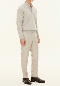 Light gray cable-knit sweater with a zip neck, paired with light gray trousers and dark brown leather boots. Smooth texture and tailored fit.