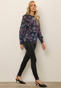 Blusa floreale a maniche lunghe in blu navy scuro e viola, abbinata a pantaloni slim in ecopelle nera e décolleté nere con punta affusolata.