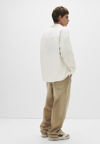 Lässiges, weißes Langarmshirt, beiger weit geschnittener Hose und Sneakers mit grünen Akzenten; schlichte Textur, keine sichtbaren Muster oder Beschläge.