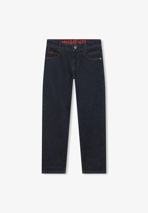 Un jean en denim bleu foncé présente une coupe droite, un design à cinq poches et des coutures de contraste. La ceinture affiche une étiquette de logo rouge.