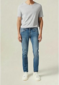 Světle šedé tričko s kulatým výstřihem v kombinaci s modrými džíny se štíhlým střihem. Bílá slip-on teniska dokončuje outfit. Hladká tkanina a klasický design.