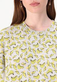 Sweatshirt cinza claro com um padrão repetido de bananas em amarelo e preto. Design clássico de gola redonda, textura suave e estilo casual.