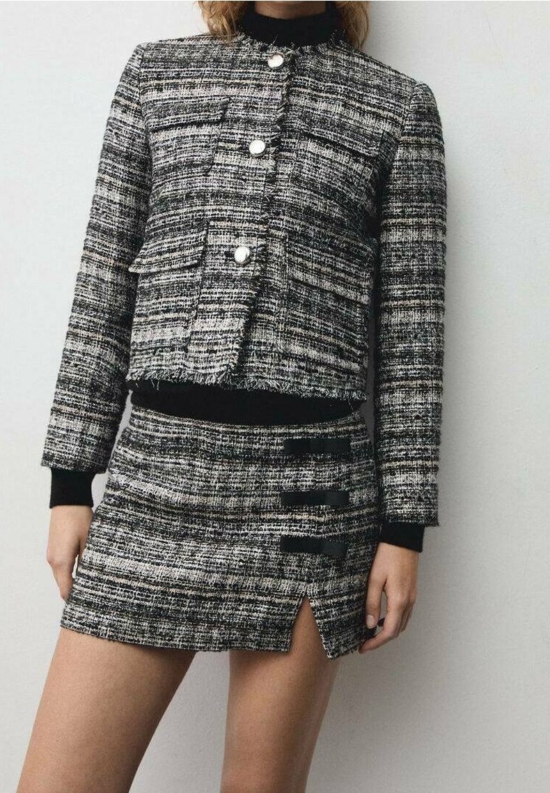 Czarna i biała kurtka w kratę tweedową o skróconym kroju, z okrągłym dekoltem i trzema guzikami. Do tego dopasowana mini spódnica z rozcięciami.