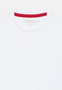 T-shirt branco com decote redondo e um destaque canelado vermelho. A textura do tecido é suave, com etiqueta de marca impressa no interior.