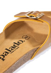 Sandal di pelle marrone con suola in sughero marrone chiaro, caratterizzato da una fibbia in metallo dorato e una soletta morbida e testurizzata etichettata "Palado, made in Spain."