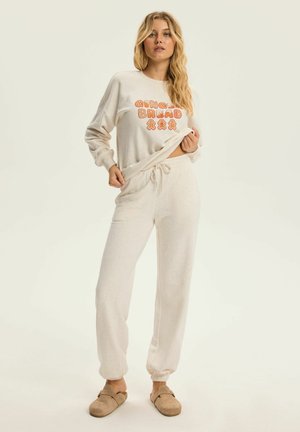 Jasnobeżowy zestaw wypoczynkowy z długim rękawem, ozdobiony grafiką "GINGER BREAD" oraz spodniami z elastycznym mankietem i sznurkiem. Miękka tekstura tkaniny.