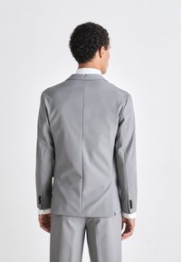 Blazer gris con una sola abertura, solapas muesca y acentos de botones negros, combinado con detalles en blanco en los puños. Textura de tela suave.