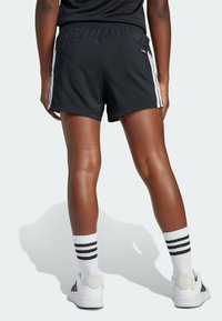 Black athletic shorts with white side stripes, elastic waistband, and a lightweight texture. Worn with white socks featuring black stripes and sneakers.
