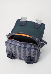 Sac en tissu navy avec un motif géométrique blanc, fermeture éclair, intérieur orange et quincaillerie argentée. Doté de doubles fermetures à boucle ajustables.