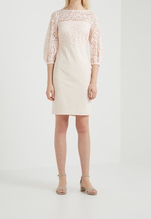 Lichtroze jurk met een kanten lijfje en driekwartmouwen, een strak aansluitende, gladde rok, gecombineerd met neutrale sandalen met blokhak.