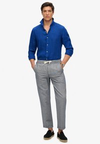 Camisa de lino azul de manga larga con botones, combinada con pantalones a rayas grises y alpargatas negras. Cuenta con una cintura elástica con cordón.